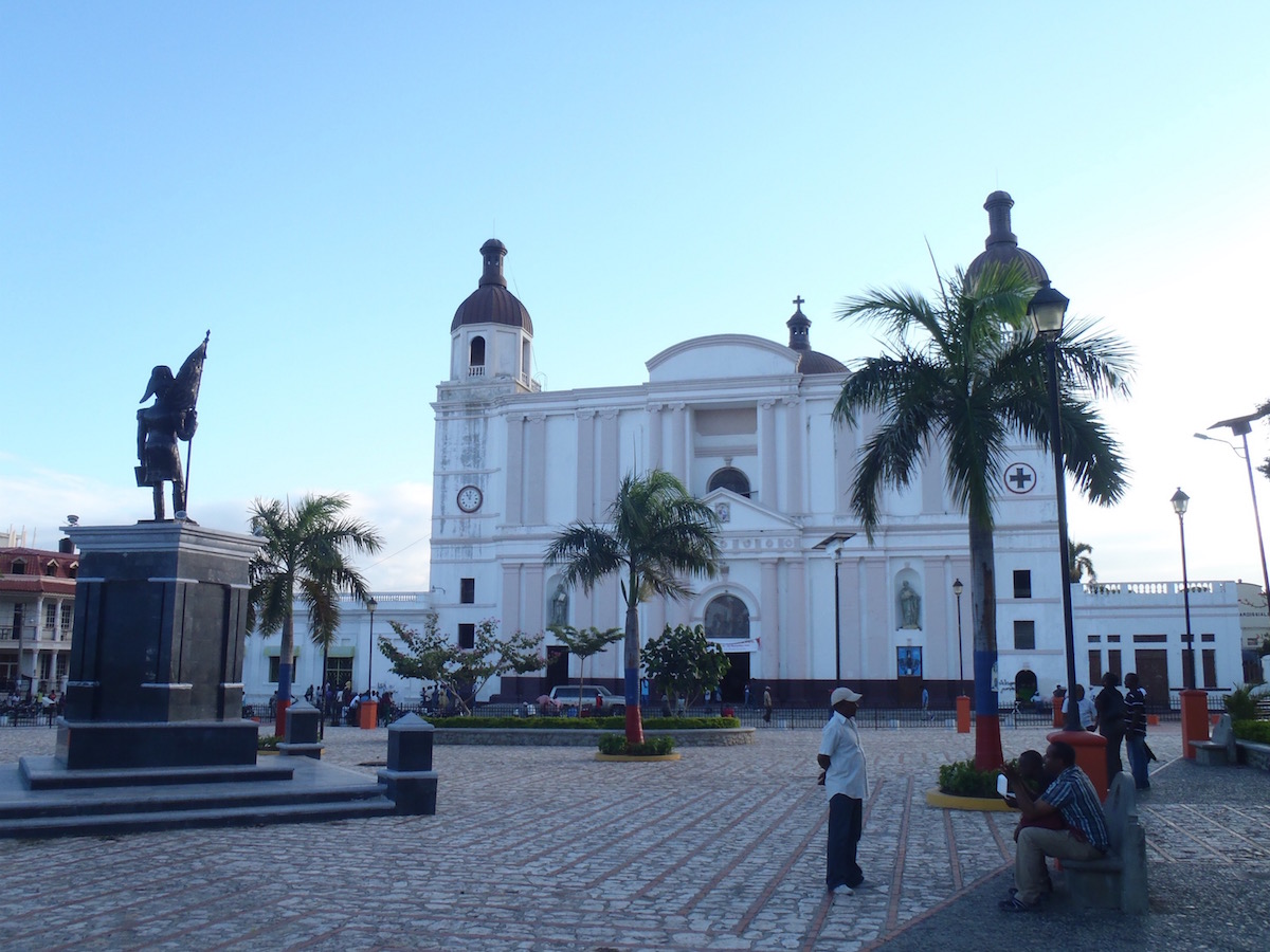 Place d'Armes in Cap-Haïtien, featuring a statue and a large building.