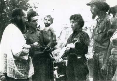 Enrique Ermus at a baptism, with woman and man holding children. 
