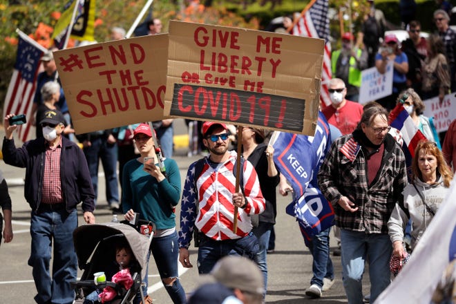 Protesters holding signs that read "#End the Shutdown" and "Give me liberty of give me COVID 19!"
