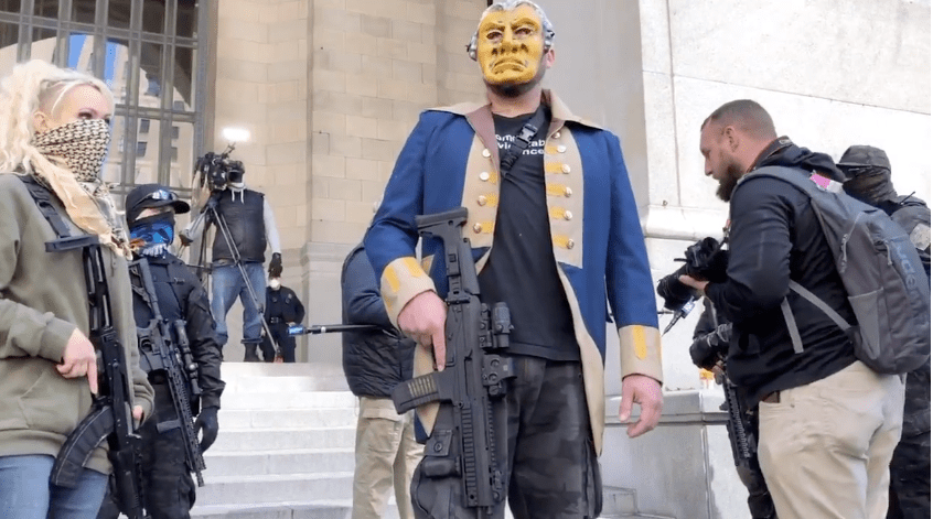 Armed protester holding a firearm and wearing a Founding Father costume.