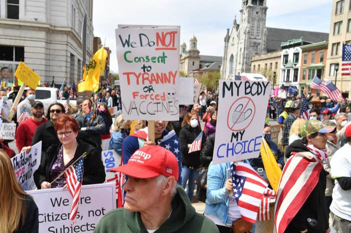 Crowd holding American flags and anti-mask and anti-vaccine signs at a protest. 