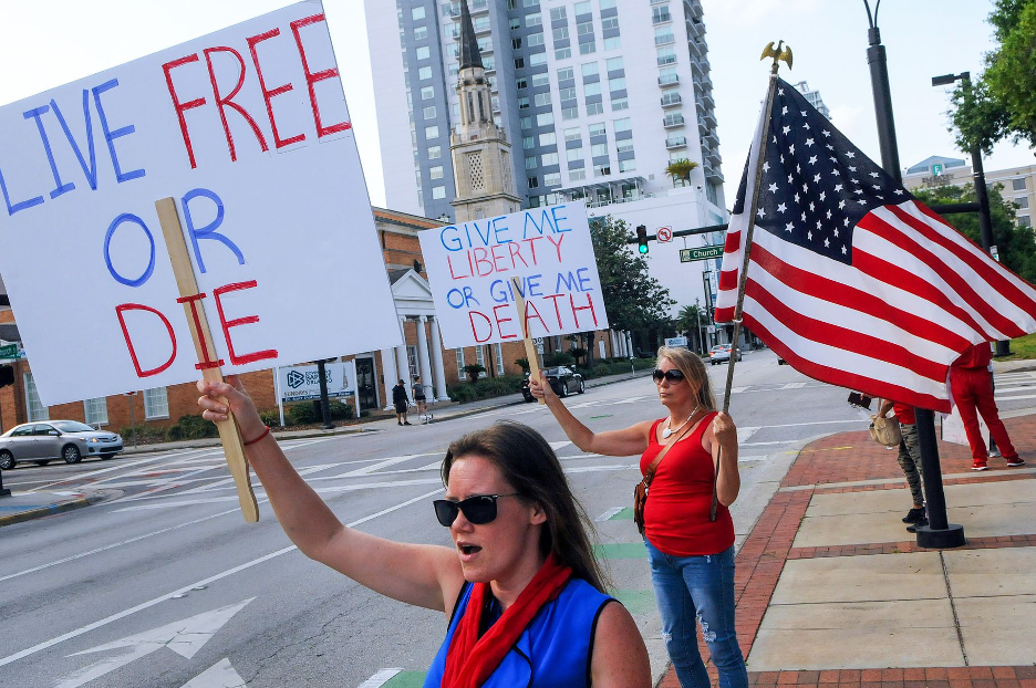 Two female protesters holding an American sign and signs that read "Live free or die" and "Give me liberty or give me death."