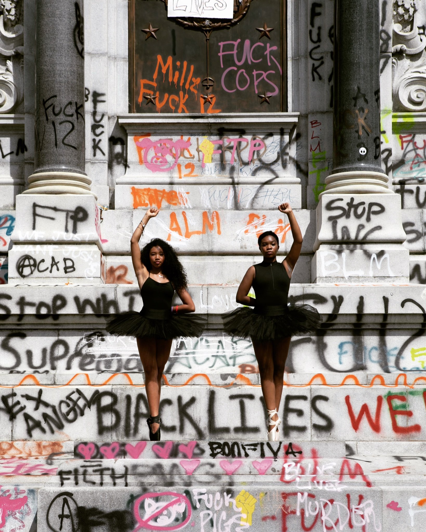 Two ballerinas posing in front of Confederate general Robert E. Lee’s monument, Richmond, Virginia, with protest graffiti.