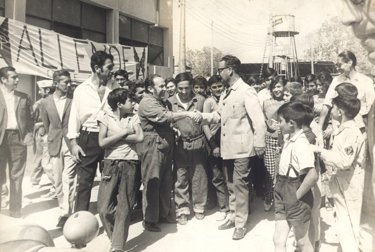 Salvaor Allende shaking hands with man in a work-suit among a crowd.