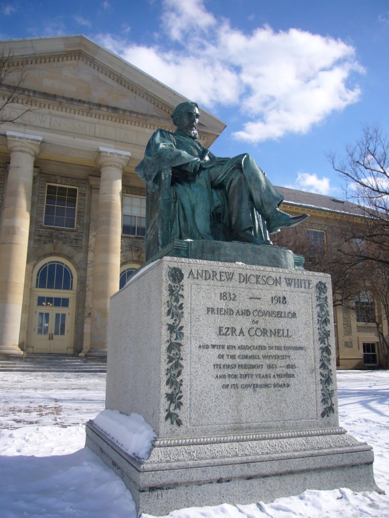 Statue of Andrew Dickson White sitting in a chair, in front a building at Cornell university.